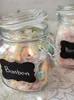 Two glass jars filled with wrapped candies, one with a lid ajar, and a small black chalkboard label attached to the front of the jar with the word "Bonbon" written on it in white. Produktbild-Vorschau