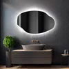 A modern bathroom vanity with a sink, faucet, and an illuminated, irregularly shaped mirror mounted on a tiled wall. Produktbild-Vorschau