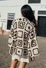 A woman wearing a crochet jacket stands outdoors on a cobblestone street in front of a white building. Produktbild-Vorschau