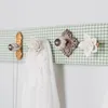 A close-up shot of decorative knobs mounted on a green gingham fabric-covered board, used as hooks. Produktbild-Vorschau