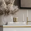 A decorative arrangement on a surface, featuring a vase with dried flowers, a gold candle holder, and books. Náhľad obrázku produktu