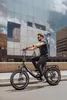 A man rides an electric bicycle in front of a modern glass building. Produktbild-Vorschau