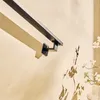 A close-up shot of a black metal handrail mounted on a beige wall, with a wooden plank casting a shadow. Podgląd zdjęcia produktu