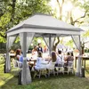 A group of people are gathered around a table under a gazebo in a garden setting. Produktbild-Vorschau