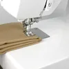 A close-up view of a sewing machine needle and foot positioned over folded tan fabric. Produktbild-Vorschau