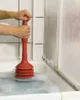 A person is using a red plunger in a bathtub filled with soapy water. Produktbild-Vorschau