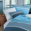 A neatly made bed with blue striped bedding and pillows, set against a backdrop of windows and a woven basket. Produktbild-Vorschau