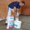 A man is preparing to mix a bag of Knauf Multi-Finish Gips-Spachtelmasse with water in a bucket. Produktbild-Vorschau