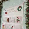 A fabric advent calendar with numbered pockets, decorated with Christmas motifs, hanging on a wall with a Christmas tree and garland in the background. Anteprima dell’immagine prodotto