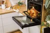 A roasted chicken is being taken out of an open oven in a modern kitchen. Produktbild-Vorschau