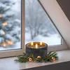A lit candle with three wicks sits on a windowsill with a snowy winter scene outside. Anteprima dell’immagine prodotto