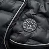 A close-up of a black quilted dog coat with a circular logo patch. Produktbild-Vorschau