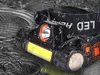 A black LED headlamp with water droplets on it, set against a dark, wet background. Anteprima dell’immagine prodotto