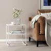 A white side table with books and a vase of flowers next to a brown leather sofa with a blanket draped over it. Podgląd zdjęcia produktu