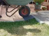 A wheelbarrow is positioned on a ramp that is placed over a curb, transitioning from a paved patio to a grassy area. Produktbild-Vorschau