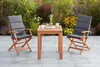 A wooden table and two chairs with cushions are set up on a patio, surrounded by plants and flowers. Náhled obrázku produktu