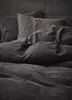 A close-up view of dark gray bedding, including pillows and a duvet, neatly arranged on a bed. Produktbild-Vorschau