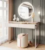 A modern vanity table with a round illuminated mirror, a stool, and decorative items in a bedroom setting. Produktbild-Vorschau