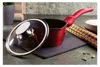 A red saucepan with a glass lid is displayed on a dark slate surface, with some spices and a bamboo mat in the background. Náhled obrázku produktu