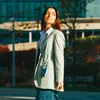 A woman walks outside wearing a blazer and jeans, with a phone attached to a lanyard around her neck. Anteprima dell’immagine prodotto