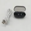 A pair of black wireless earbuds in an open charging case, next to a white USB charging cable, on a white and gray surface. Voir les images du produit