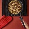A hand is holding a pan handle, with a baking pan filled with cookie dough and chocolate chunks on an oven rack. Podgląd zdjęcia produktu
