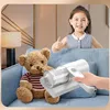 Weißer Handstaubsauger, von einer Hand gehalten, reinigt ein blaues Sofa neben einem Teddybären, im Hintergrund lächelt ein Kind und gibt ein Daumen hoch Anteprima dell’immagine prodotto