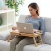 A woman is sitting on a couch using a laptop on a portable table. Produktbild-Vorschau