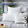 Three white quilted pillows are arranged on a light gray sofa in a living room setting. Produktbild-Vorschau