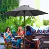 Three women sitting at a table under a large gray umbrella at an outdoor cafe. Produktbild-Vorschau