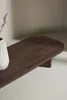 A close-up shot of a modern, dark wood coffee table with a textured white vase and dried plant on its surface. Produktbild-Vorschau
