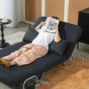 A person is lying on a dark gray sofa bed, reading a magazine. Náhled obrázku produktu