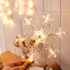 A hand holding a snowflake-shaped LED light decoration, with other similar decorations and blurred background elements suggesting a festive or decorative setting. Produktbild-Vorschau