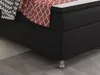 A close-up view of a black box spring bed with a red and white patterned throw blanket and a black and white patterned pillow. Produktbild-Vorschau