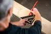 A person is using a triangular ruler to mark a wooden plank. Voir les images du produit