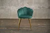 A green velvet chair with gold legs stands on a wooden floor in front of a concrete wall. Produktbild-Vorschau