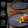 A close-up shot of two dark gray dinner plates on a wooden table, one with food and a flower, and informational icons on the left. Produktbild-Vorschau