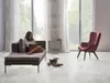 A woman is reading a book on a chaise lounge in a bright, modern living room with large windows. Produktbild-Vorschau