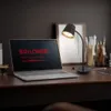 A laptop and a desk lamp are on a wooden desk, with art supplies in the background. Náhľad obrázku produktu