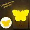 A yellow butterfly-shaped LED night light is plugged into a wall socket. A smaller inset image shows the same night light on a white circular background. Produktbild-Vorschau