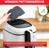 A hand is holding a charcoal filter over an air fryer. The background is a kitchen counter with jars and plants. Produktbild-Vorschau