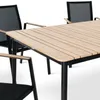 A close-up view of a wooden slatted tabletop and black metal legs of a dining table, with parts of two chairs visible. Produktbild-Vorschau