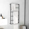 A black metal towel rack with two white towels hanging on it, placed against a marble-patterned wall in a bathroom. A white vanity with a soap dispenser and a small dish is visible to the left. A wicker basket with towels is in the lower right corner. Náhľad obrázku produktu