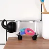 A clear plastic container with a black elephant-shaped lid sits on a wooden surface, holding colorful hair ties. The background is a white tiled wall. Náhľad obrázku produktu