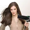A woman is holding a black hairdryer with green accents. Produktbild-Vorschau