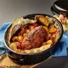 A roasted meat dish with potatoes and orange slices in a black oval roasting pan, lined with parchment paper. Podgląd zdjęcia produktu