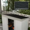 A close-up view of a metal shed roof with a textured black surface, set against a backdrop of trees and a stone wall. Podgląd zdjęcia produktu