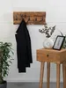 A black jacket hangs on a wooden coat rack mounted on a white brick wall, next to a wooden side table with a vase and a framed picture. Náhľad obrázku produktu