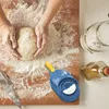 Hands kneading dough on a wooden board, with a dumpling maker tool and jars in the background. Podgląd zdjęcia produktu