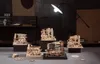 A collection of wooden mechanical models, likely marble runs or similar intricate kits, displayed on a table in a dimly lit room with a spotlight. Voir les images du produit